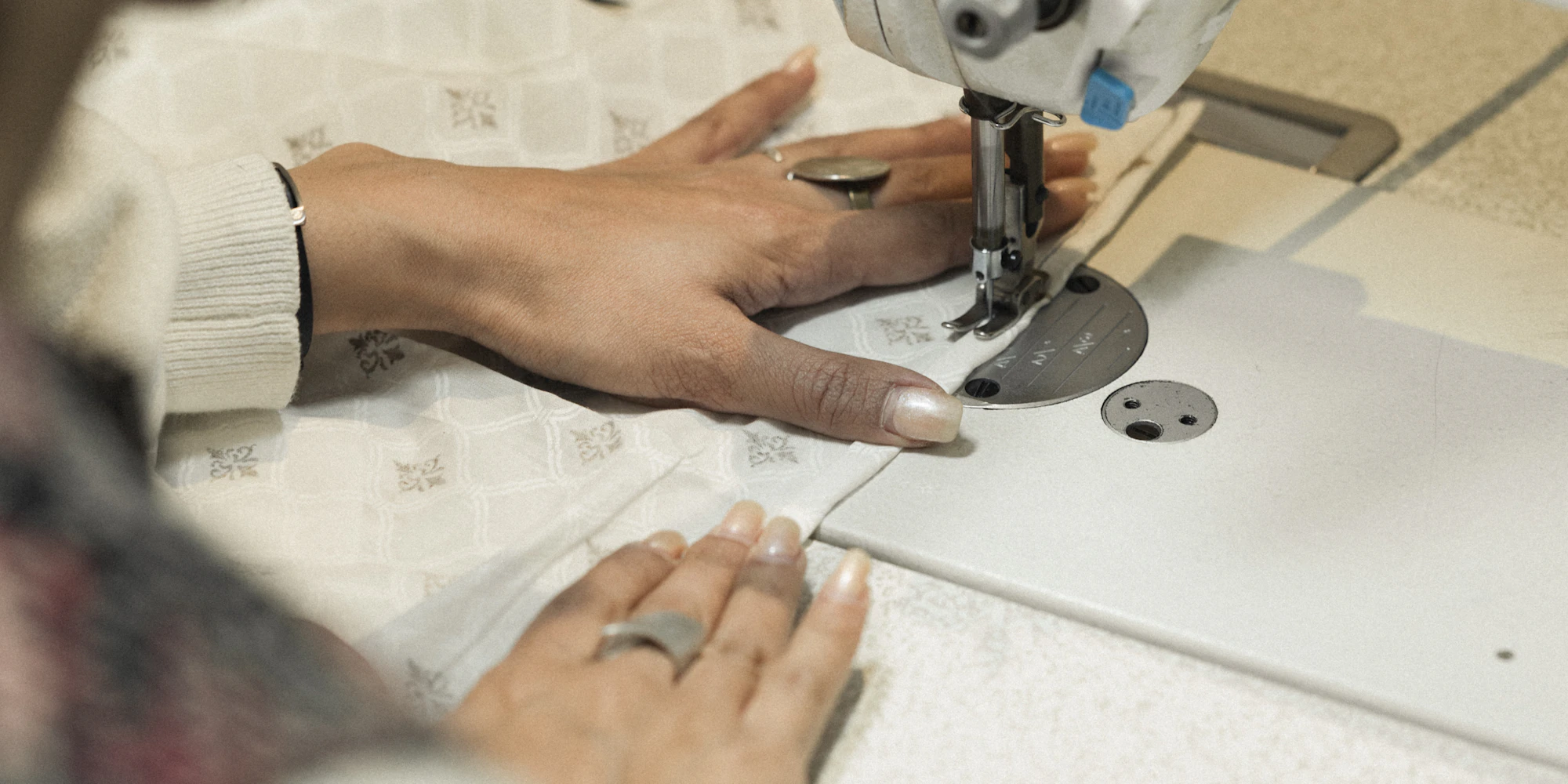 Imagem ilustrativa de mãos guiando tecido sob a agulha de uma máquina de costura